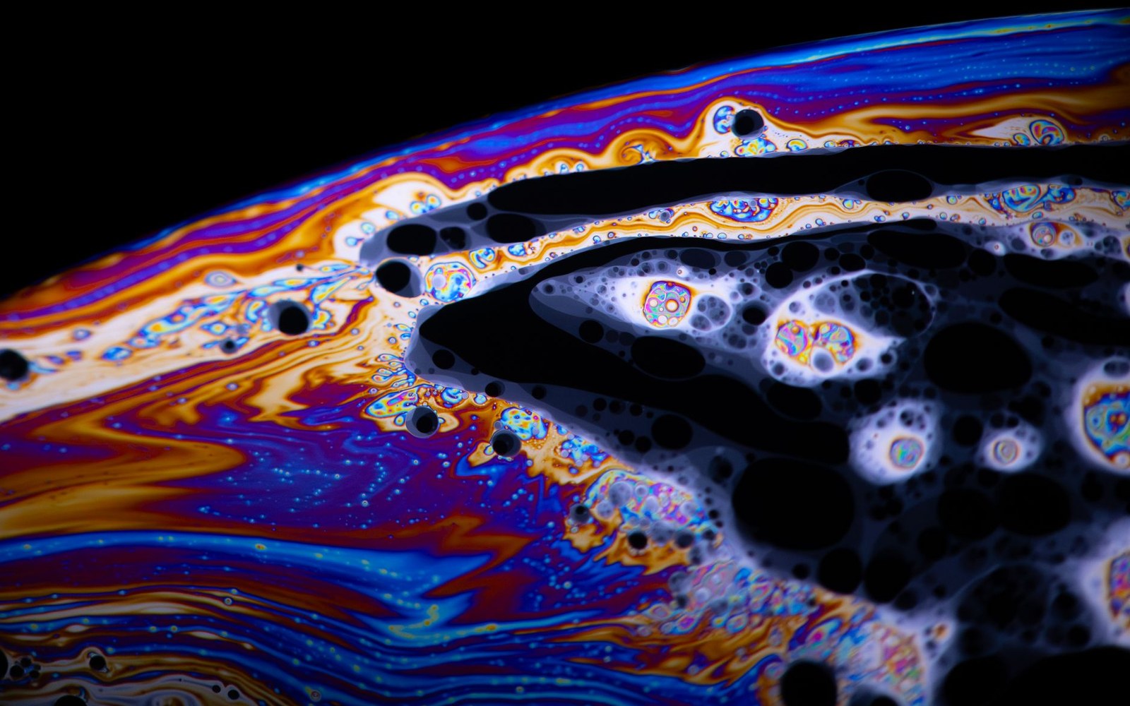 Close-up of a soap bubble's swirling rainbow film with dark bursting patches