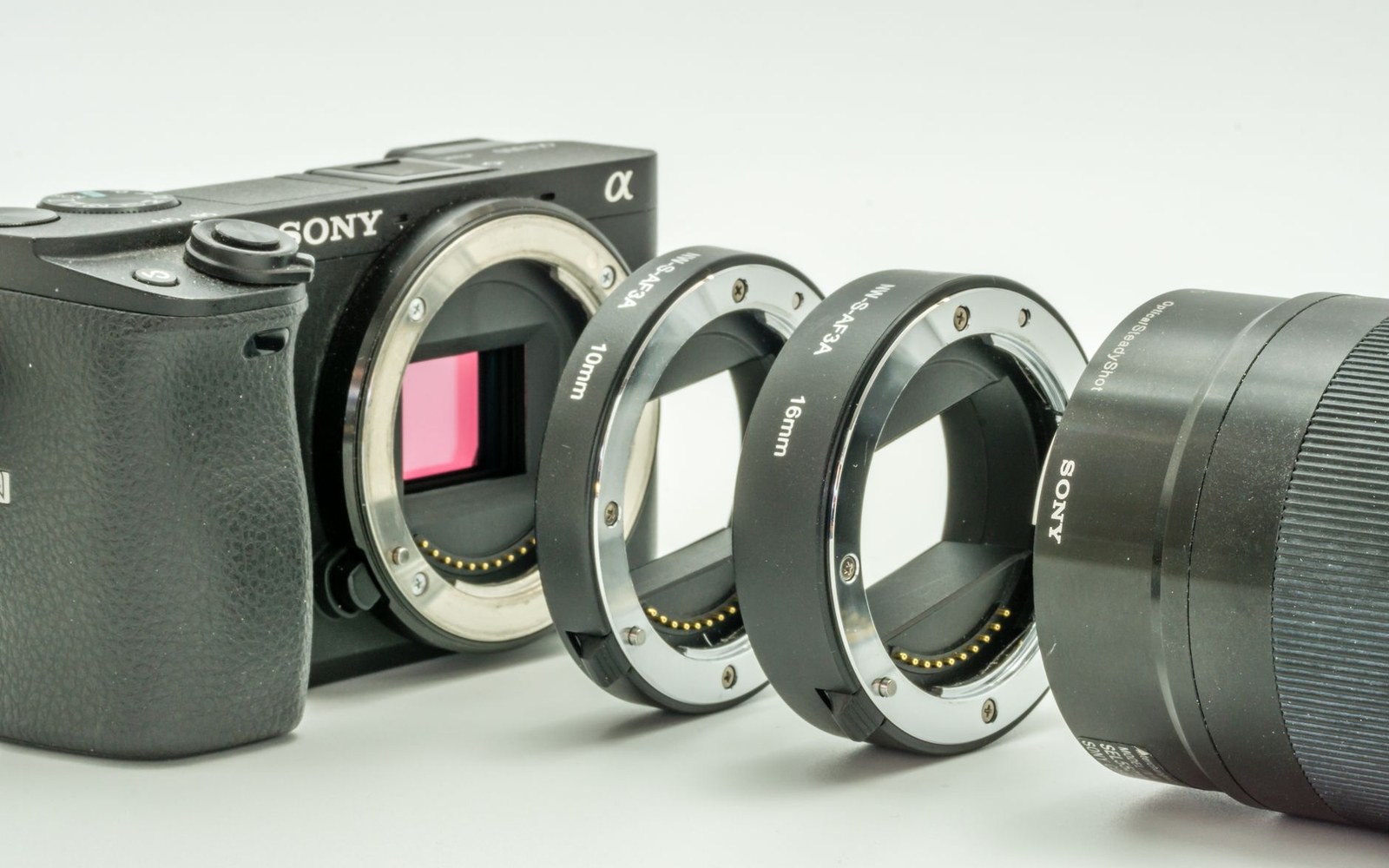 Sony mirrorless camera body with lens extension tubes and a detached lens lined up beside it