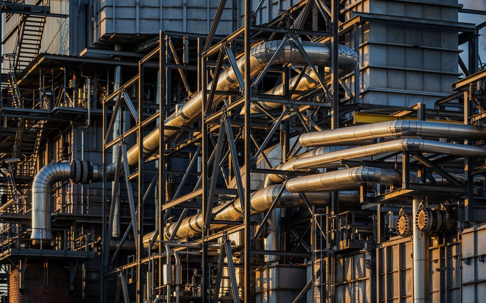 Metal pipes and steel scaffolding crisscross an industrial refinery structure at sunset