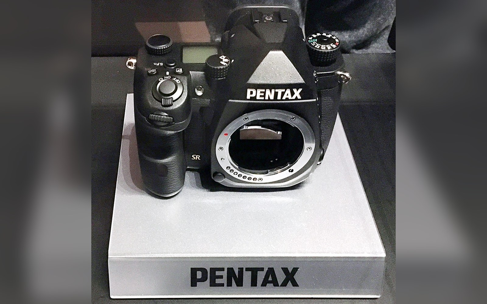 Pentax K-3 Mark III body, black, three-quarter view on grey card, K-mount contacts visible