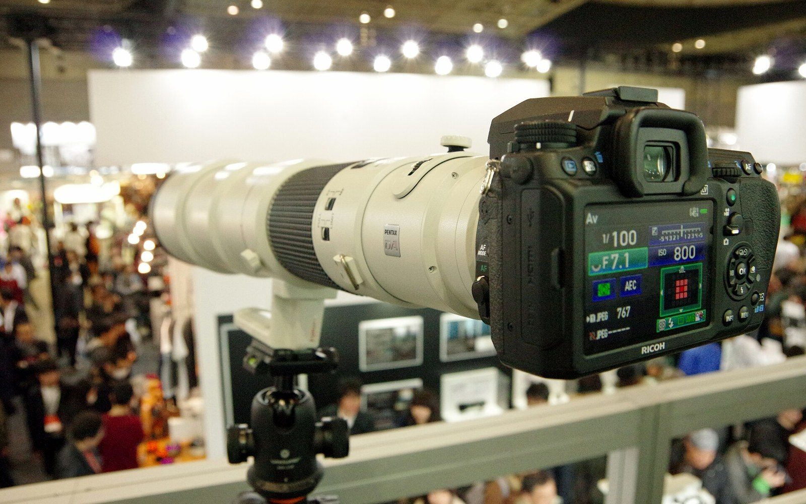 Pentax HD DA lens cross-section display showing internal element groups, mounted on a grey panel